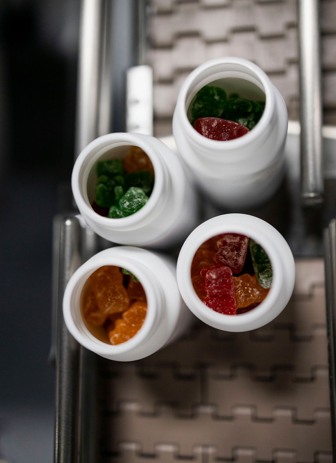 Four open white bottles of colorful gummies on a conveyor